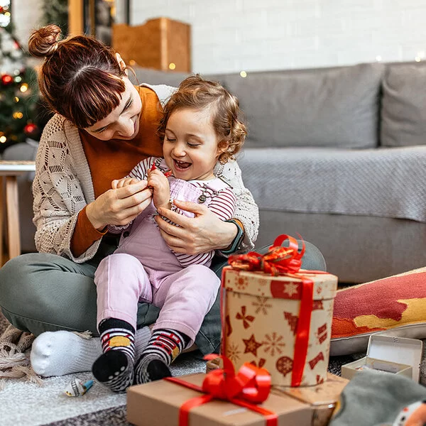 Ein kleiens Kind sitzt mit seiner Mutter auf dem Boden und öffnet mit ihr Weihnachtsgeschenke.