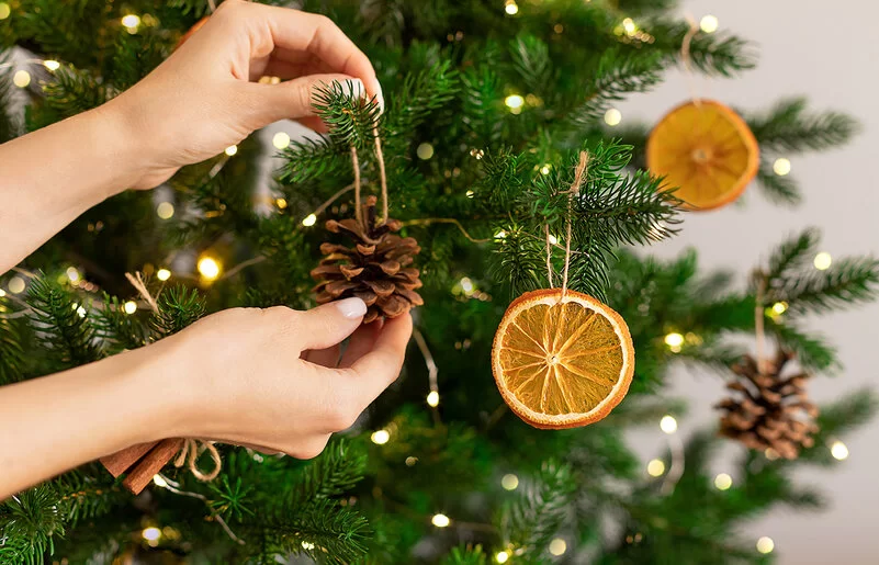 Frauenhände hängen Weihnachtsschmuck an einen Tannenbaum.