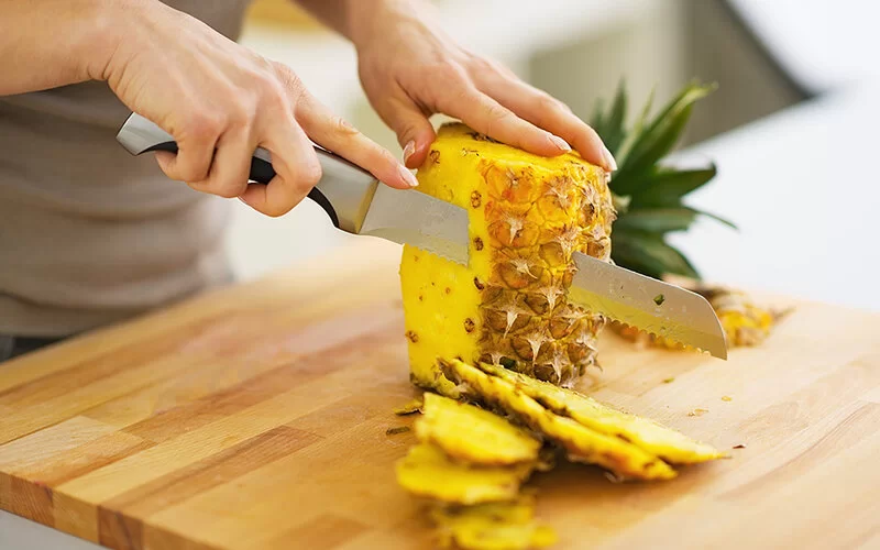 Nahaufnahme einer Ananas, die eine Frau mit einem Messer schält.