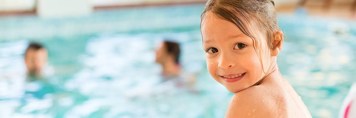  Kind sitzt im Schwimmbad am Beckenrand