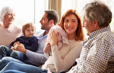 Drei Generationen einer Familie sitzen gemeinsam auf einer Couch und unterhalten sich angeregt.