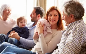 Drei Generationen einer Familie sitzen gemeinsam auf einer Couch und unterhalten sich angeregt.