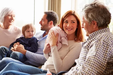 Drei Generationen einer Familie sitzen gemeinsam auf einer Couch und unterhalten sich angeregt.