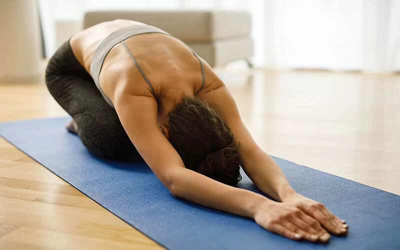 Eine Frau kniet auf einer Gymnastikmatte. Sie legt dabei den Kopf und die Hände auf der Matte ab.