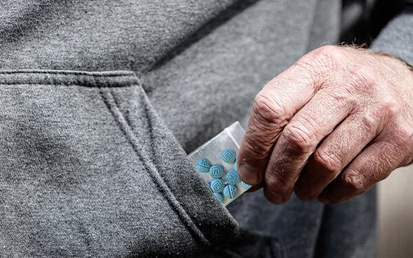 Blaue Pillen in einer kleinen Plastiktüte, die von einer Männerhand in Nahaufnahme aus einer Jackentasche gezogen wird.