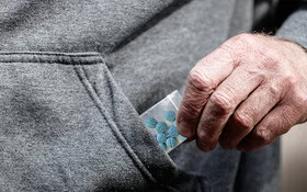 Blaue Pillen in einer kleinen Plastiktüte, die von einer Männerhand in Nahaufnahme aus einer Jackentasche gezogen wird.