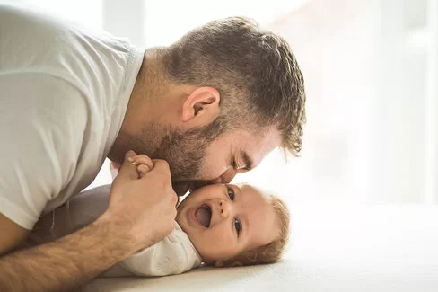 Ein Mann küsst ein Baby, das mit dem Rücken auf einem Wickeltisch liegt. 