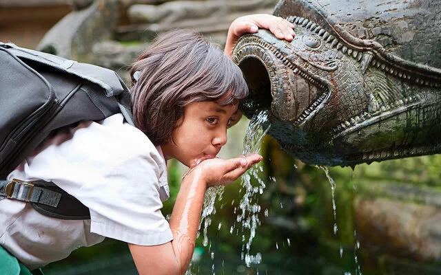 Ein junges Mädchen trinkt mit der Hand aus einem Brunnen.