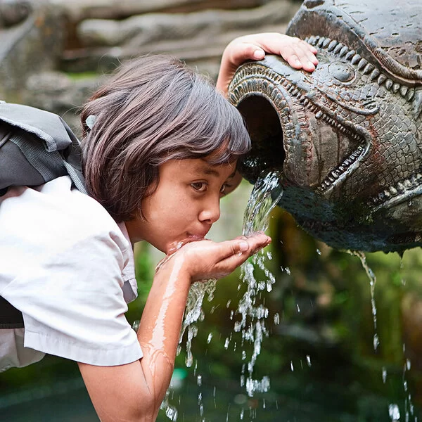 Ein junges Mädchen trinkt mit der Hand aus einem Brunnen.