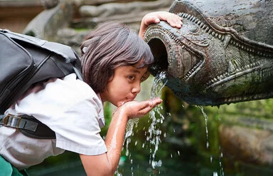 Ein junges Mädchen trinkt mit der Hand aus einem Brunnen.