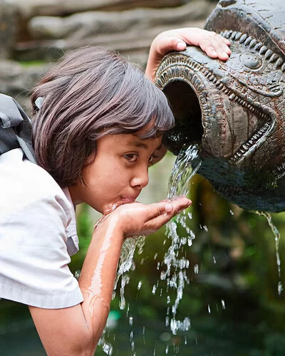 Ein junges Mädchen trinkt mit der Hand aus einem Brunnen.