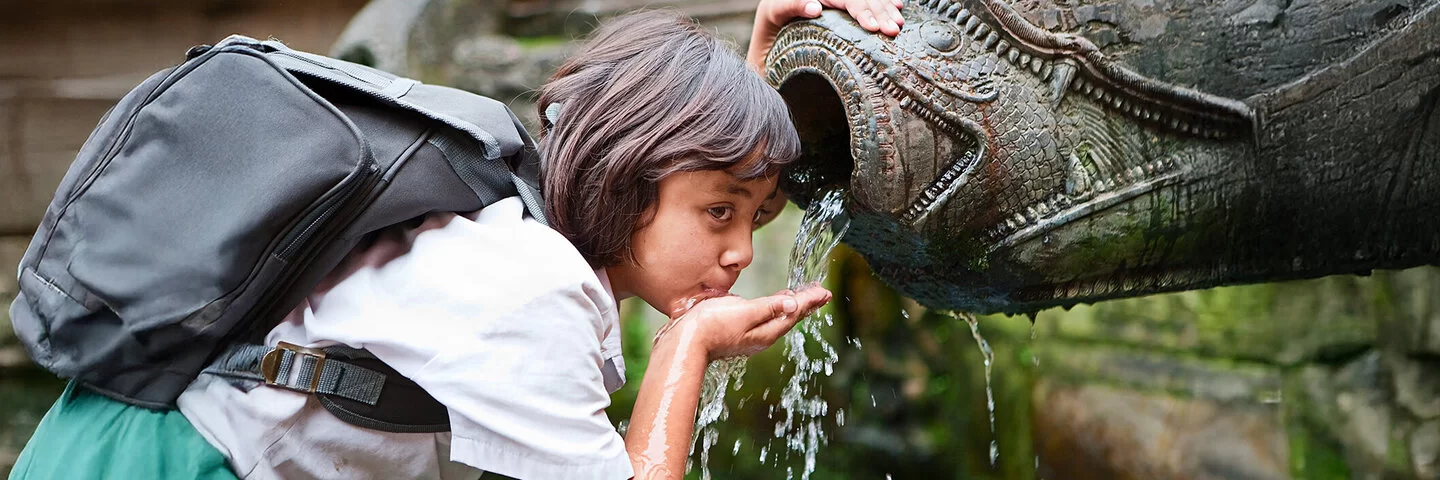 Ein junges Mädchen trinkt mit der Hand aus einem Brunnen.