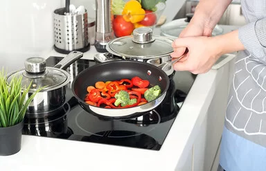 Eine Person stellt eine Pfanne mit Gemüse auf den Herd.