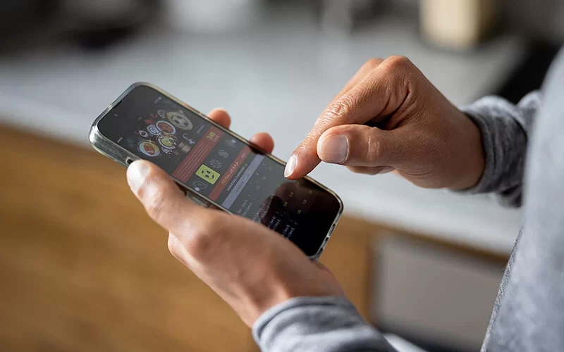 Groß zu sehen ist der rechte Zeigefinger eines Mannes. Damit tippt er etwas auf dem Smartphone ein. Er hat sich eine App heruntergeladen und nimmt an einer Sportwette teil.