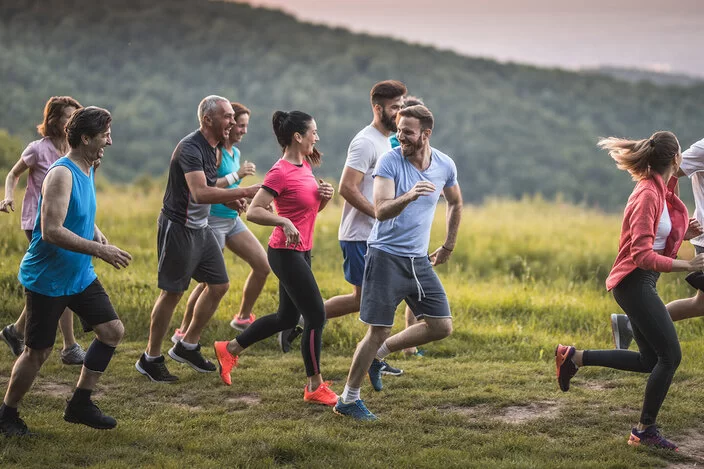 Eine Gruppe Menschen gemischten Alters joggt durch die Natur und lacht gemeinsam.