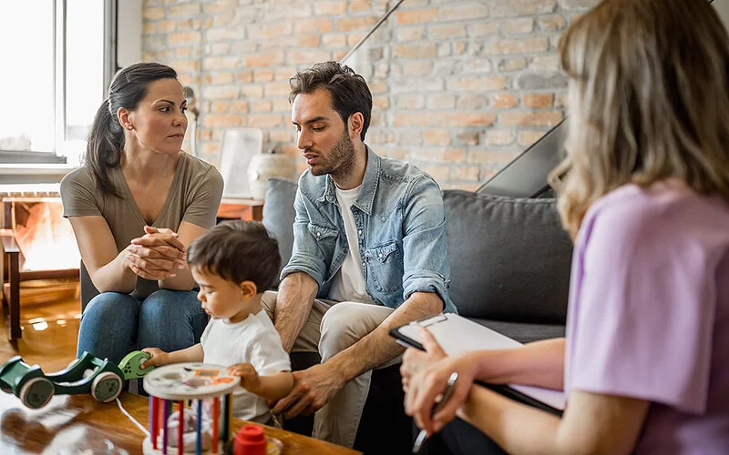 Ein junges Paar mit einem ungefähr dreijährigen Jungen sitzt auf einem Sofa bei einer Familientherapeutin.