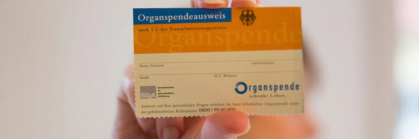 Eine Frau hält einen Organspendeausweis in die Kamera, ihr Gesicht ist verschwommen.