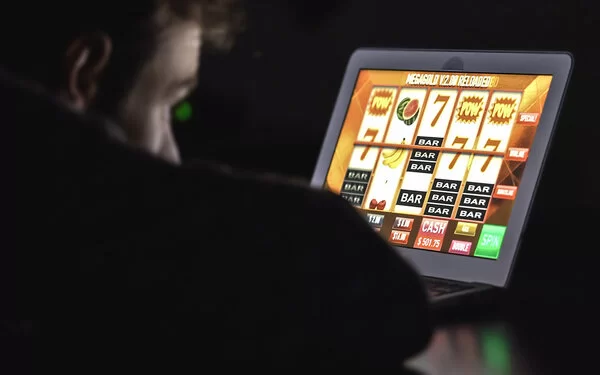 Eine nicht erkennbare Person sitzt im Dunkeln vor einem Notebook und schaut auf ein Glücksspiel eines Online-Casinos.