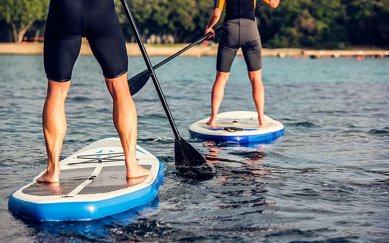 Zwei Personen stehen breitbeinig auf einen breitem Board für SUP.