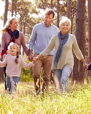 Fröhliche Mehr-Generationen-Familie hält sich an den H#änden und läuft über eine Wiese im Wald.