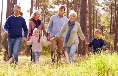 Fröhliche Mehr-Generationen-Familie hält sich an den H#änden und läuft über eine Wiese im Wald.