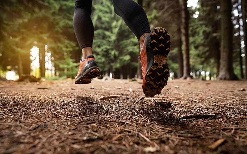 Eine Person mit läuft mit Joggingschuhen über Waldboden.