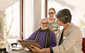 Ein altes Paar spricht mit einer Pflegeberaterin der AOK. Die Pflegeberaterin erklärt in einem Beratungsgespräch, wie sich die Pflege organisieren lässt.