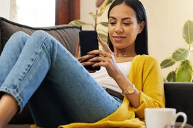 Eine junge Frau sitzt auf einem Sofa und schaut auf ihr Smartphone.