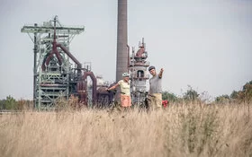 Zwei Radfahrer stehen am Rand einer vertrockneten Wiese vor der Hattingen-Henrichshütte.