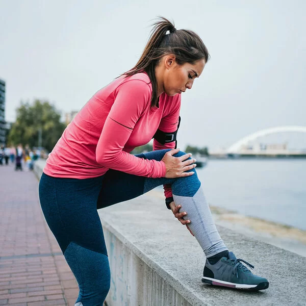 Eine Frau hält sich beim Joggen das Knie vor Schmerzen.