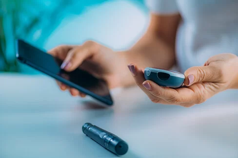 Eine Frau hält ein Blutzuckermessgerät in der Hand und überprüft ihre Blutzuckerwerte mobil auf dem Smartphone.