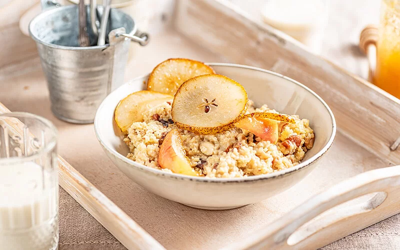 Eine kleine Schüssel mit süßer Hirsegrütze und Obst steht auf einem Holztablett. 