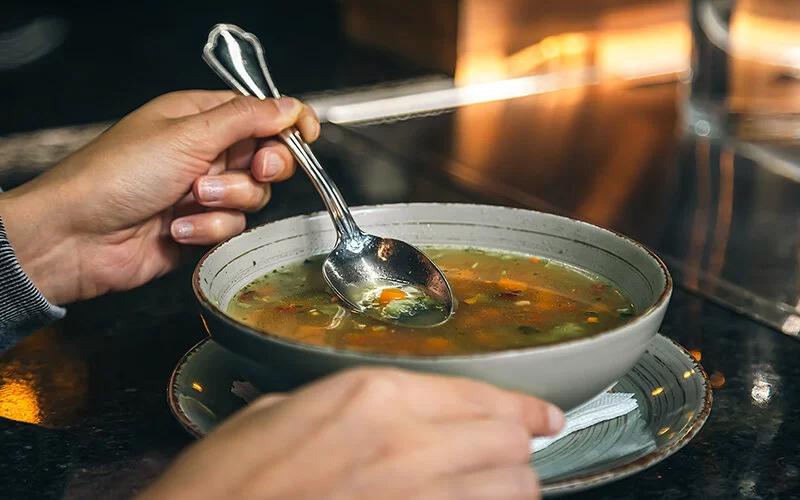 Eine Frau sitzt in einem Café und isst mit einem Löffel eine Gemüsesuppe.