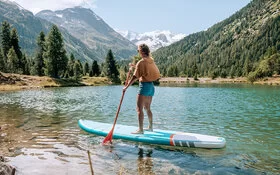 Eine junge Frau macht Stand-up-Paddling auf einem Bergsee.