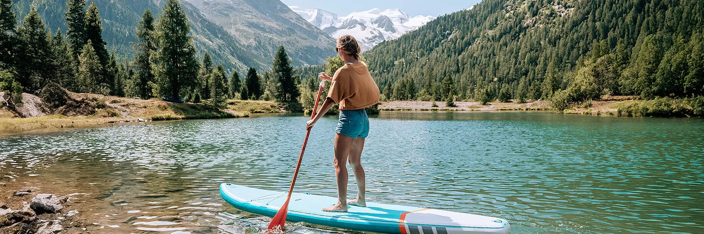 Eine junge Frau macht Stand-up-Paddling auf einem Bergsee.