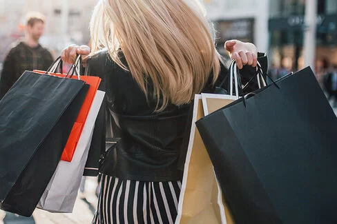 Eine Frau trägt mehrere Einkaufstaschen über den Schultern und schlendert durch eine Einkaufsstraße zum Shoppen
