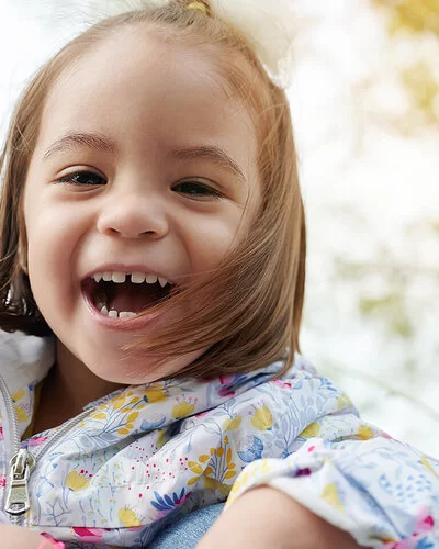 Ein fröhlich lächelndes, etwa drei Jahre altes Mädchen mit einer Zahnlücke zwischen den Schneidezähnen.