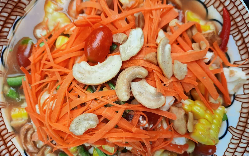 Ein bunter Salatteller mit geraspelten Möhren, Mais und grünen Bohnen, der mit Cashewkernen garniert ist.