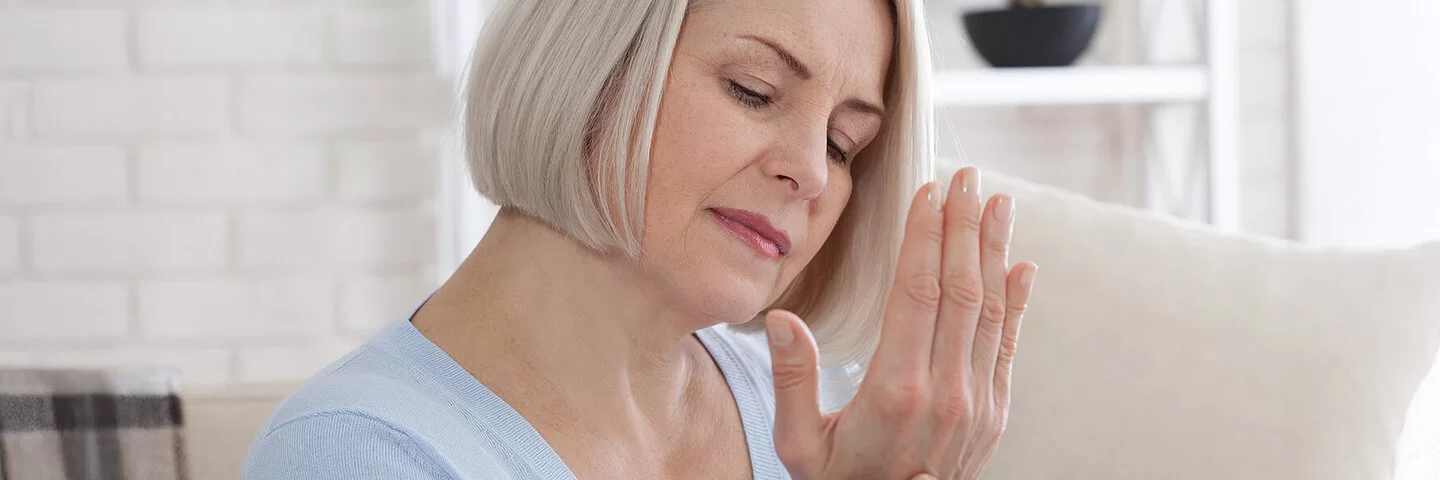 Ältere Frau massiert sich die Finger, weil sie unter Gicht leidet.