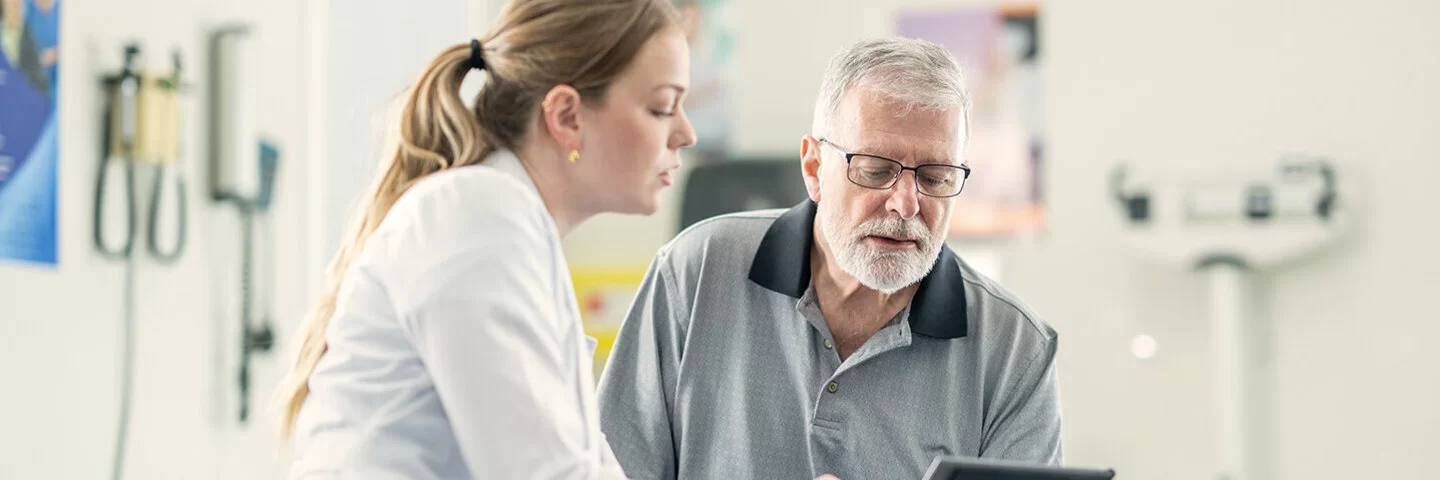 Eine Ärztin zeigt einem älteren männlichen Patienten im Behandlungszimmer medizinische Befunde und bespricht diese mit ihm.