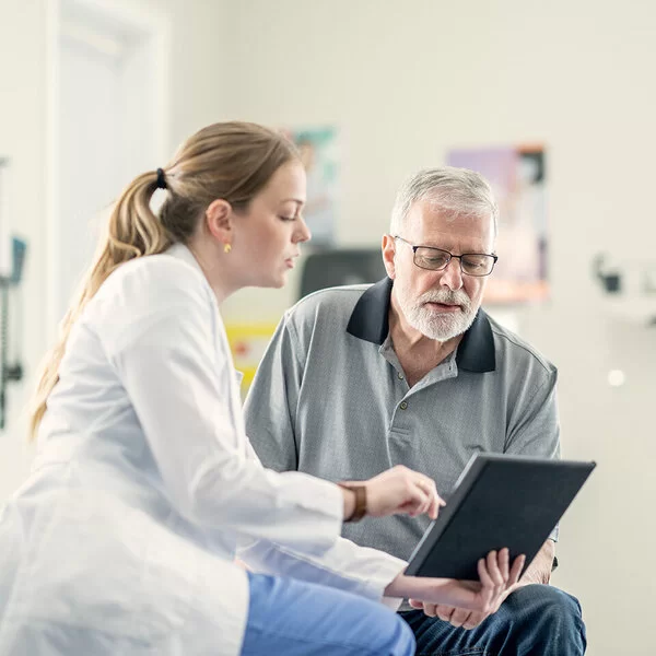 Eine Ärztin zeigt einem älteren männlichen Patienten im Behandlungszimmer medizinische Befunde und bespricht diese mit ihm.