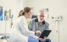 Eine Ärztin zeigt einem älteren männlichen Patienten im Behandlungszimmer medizinische Befunde und bespricht diese mit ihm.