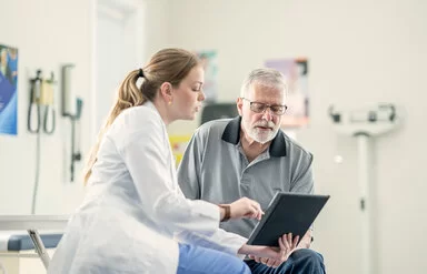 Eine Ärztin zeigt einem älteren männlichen Patienten im Behandlungszimmer medizinische Befunde und bespricht diese mit ihm.