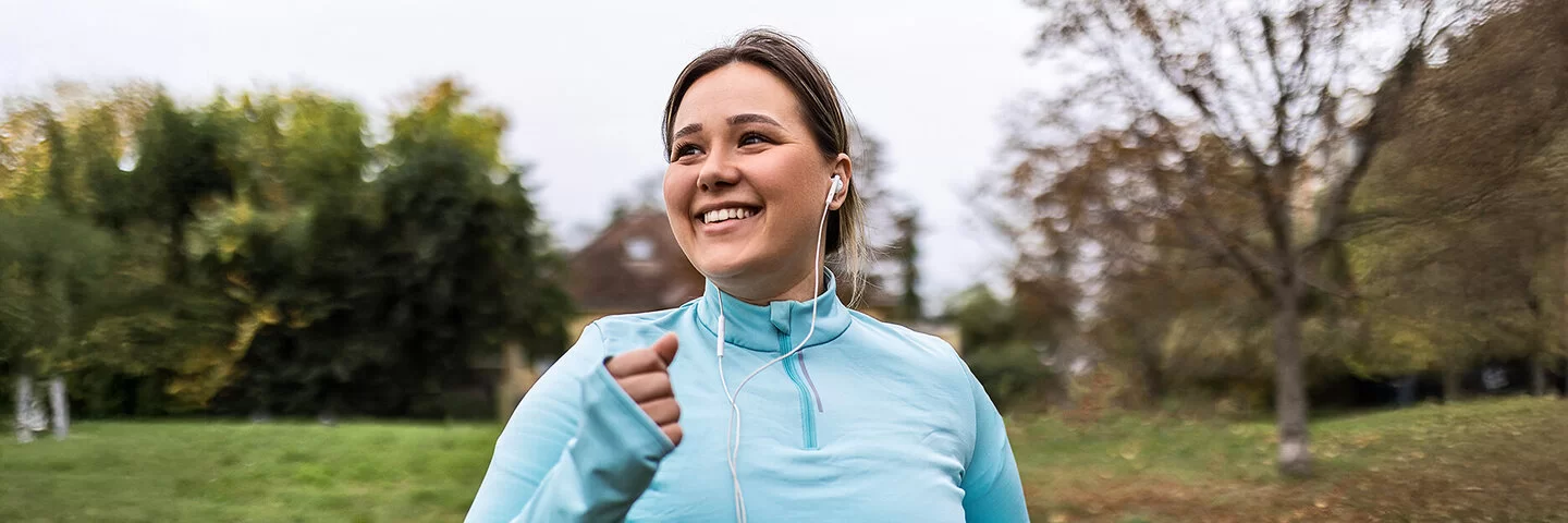 Eine junge Frau joggt durch einen herbstlichen Park. Sie hat Spaß an Sport und Bewegung.