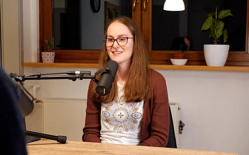 Eine weibliche Person sitzt an einem Tisch und spricht in eine Podcast-Mikrofon.