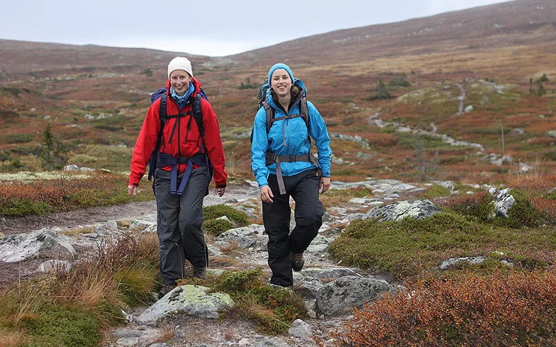 Zwei Frauen in Wanderausrüstung wandern durch eine karge, felsige Landschaft.