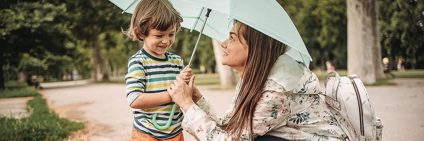 Eine junge Mutter mit ihrem Sohn lächelnd unter einem Regenschirm in einer Pfütze.