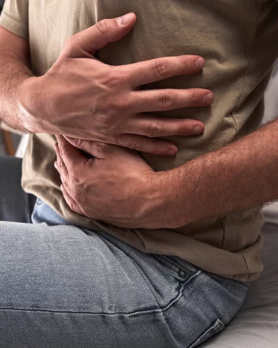 Ein sitzender Mann in einem olivgrünen T-Shirt hält sich mit den Händen die linken Rippen.