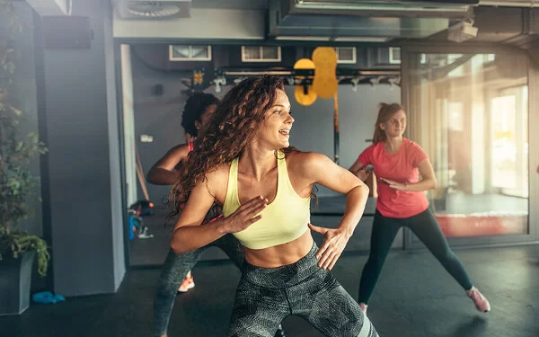 Drei Frauen in Sportkleidung beim Zumba in einem Fitnessstudio.