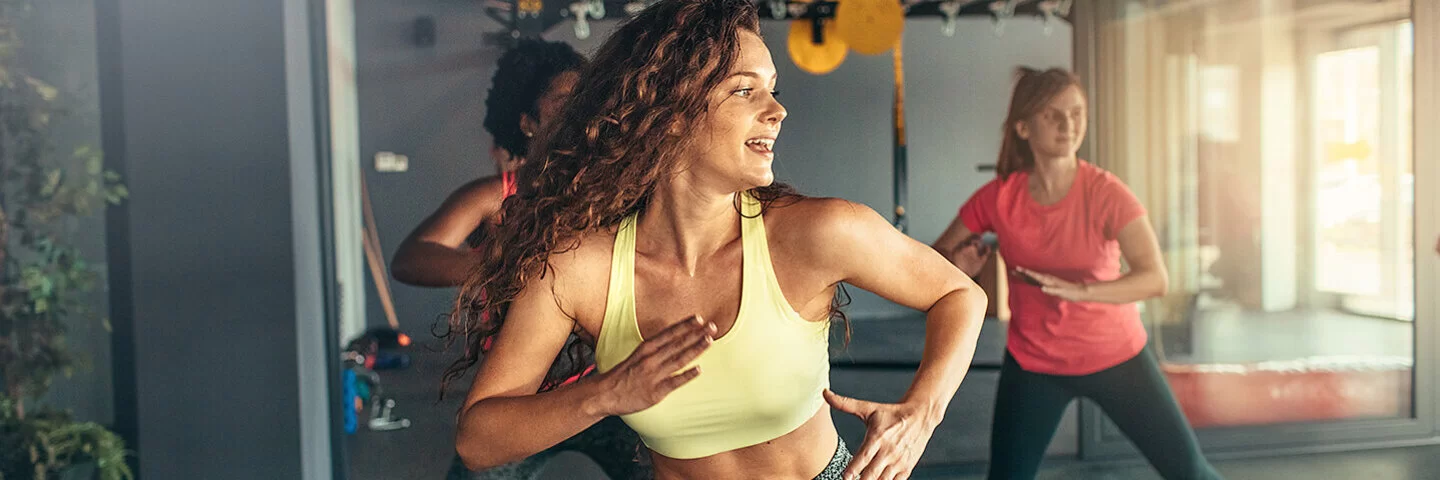 Drei Frauen in Sportkleidung beim Zumba in einem Fitnessstudio.